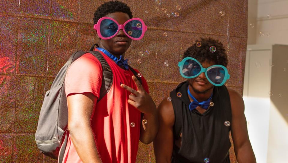 两名学生戴着超大的太阳镜，在闪闪发光的背景前合影